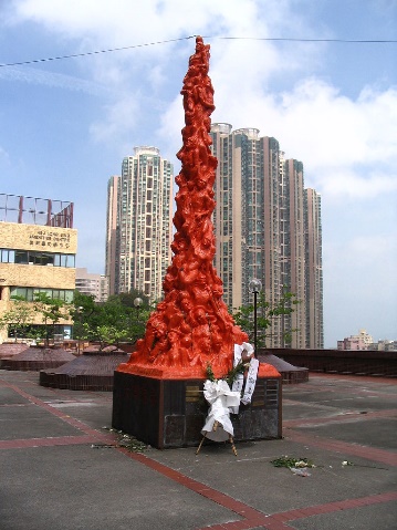 A picture of the tall thin vertical sculpture featuring  many figures smashed together all in red